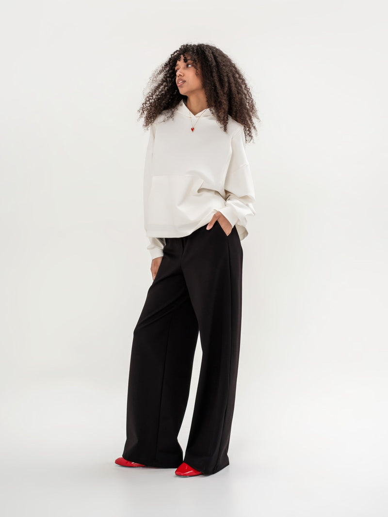 White hoodie with a zipper in the shoulder area on the back and  black wide leg trousers