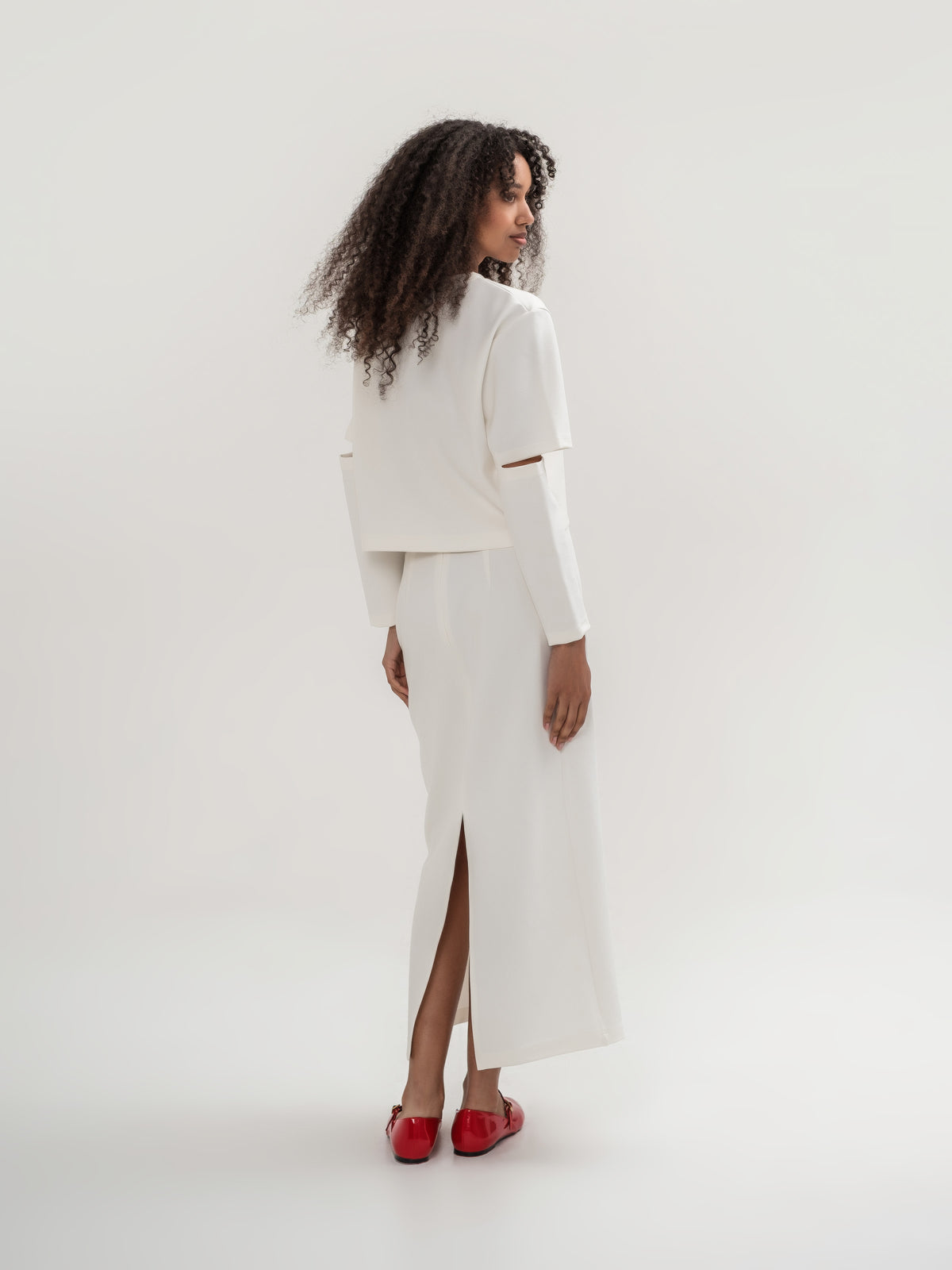 White top with slits in the elbow area and white straight long skirt with slit on the back