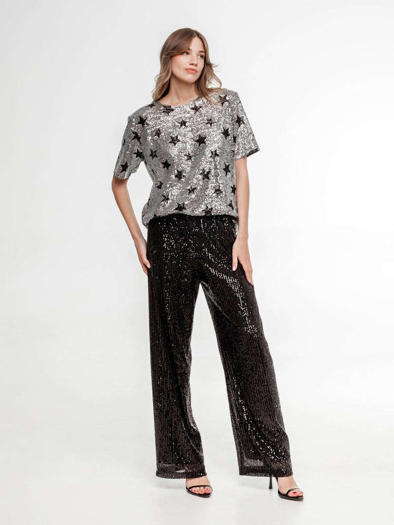 silver glitter top with stars and black glitter wide pants on the model